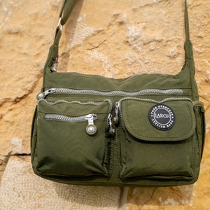 May include: A green nylon crossbody bag with multiple zippered pockets and a black circular patch that reads "YOUR EVERYDAY LARCH STYLISH BAGS".