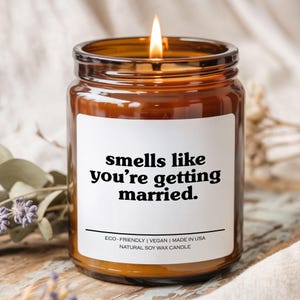 May include: A lit, brown glass jar candle with a white label. The label reads "smells like you're getting married." The candle is labeled "ECO-FRIENDLY | VEGAN | MADE IN USA NATURAL SOY WAX CANDLE."