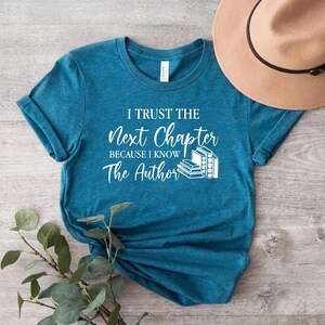 May include: Teal blue t-shirt with white text that reads "I trust the next chapter because I know the author". The text is accompanied by a graphic of a stack of books.