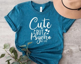 May include: A teal blue t-shirt with the text "Cute but Psycho" in white lettering. The text "But Cute" is written in smaller white lettering below the main text.
