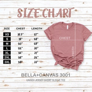 May include: Size chart for a unisex jersey short sleeve tee. The chart shows the chest and length measurements in inches for sizes XS to 3XL. The chart is printed on a wooden surface. The image also shows a pink t-shirt.
