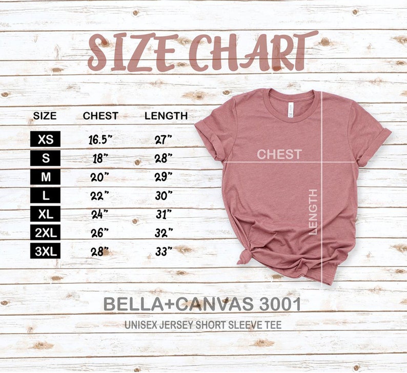 May include: Size chart for a unisex jersey short sleeve tee. The chart shows the chest and length measurements in inches for sizes XS to 3XL. The chart is printed on a wooden surface. The image also shows a pink t-shirt.