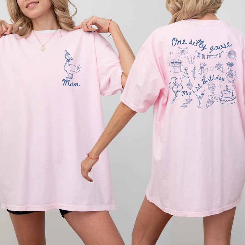 Peut inclure: T-shirt rose clair avec un dessin d'oie bleue portant un chapeau de f&ecirc;te et le mot "Mom" imprim&eacute; en dessous. Le dos du t-shirt porte l'inscription "One silly goose Mia's 1st Birthday" avec diverses illustrations bleues, dont des ballons et un g&acirc;teau.