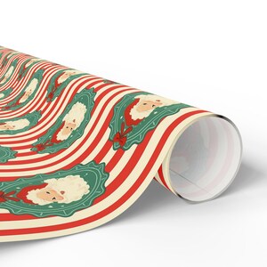 May include: Rolled wrapping paper featuring a repeating pattern of Santa Claus faces within green frames, set against a backdrop of red and cream-colored stripes. The design includes a red bow. Ideal for Christmas gifts.