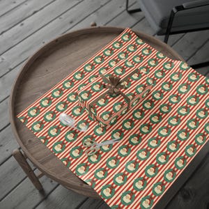 May include: A wrapped gift with a brown ribbon sits on wrapping paper featuring red and white stripes and Santa Claus wreath patterns. Scissors and tape are also on the paper, suggesting gift wrapping.