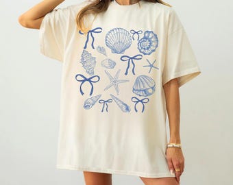 May include: A cream colored oversized t-shirt with a blue seashell and bow print. The text "IVORY SHIRT" is at the bottom of the image.