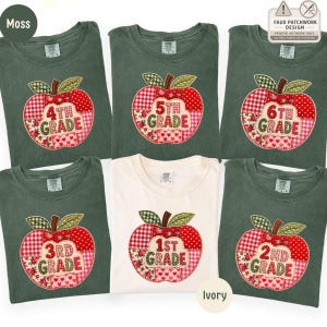 May include: A collection of six t-shirts in moss green and ivory, each featuring a printed faux patchwork apple design. The apples are composed of red, white, and pink patterned segments with text indicating grade levels from 1st to 6th grade.