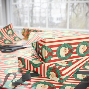 May include: Christmas-themed gift boxes wrapped in red and cream striped paper with Santa Claus medallions. A roll of matching wrapping paper and scissors are visible, along with a black ribbon. The scene is set on a table near a window.