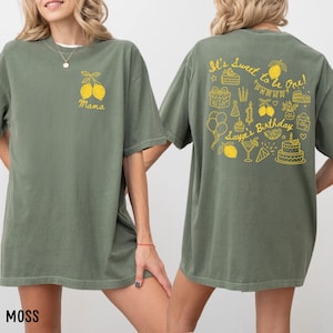 Könnte beinhalten: Moosgrünes T-Shirt mit gelber Zitronengrafik und dem Wort "Mama" auf der Vorderseite. Auf der Rückseite steht der Text "It's Sweet to be One!" mit Geburtstagsillustrationen, darunter Kuchen, Luftballons und "Layla's Birthday".