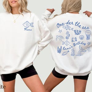 May include: White sweatshirt with blue sea-themed illustrations. The front has a fish and the word "Mama". The back shows sea creatures and the text "One-der the sea" and "Emma's Birthday".