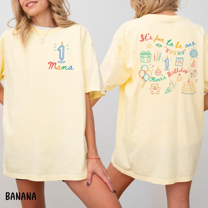 May include: A light yellow t-shirt with the word "Mama" and a number one candle graphic on the front. The back of the shirt has the text "It's fun to be one" with birthday-themed illustrations. The shirt is a casual style.