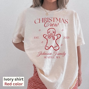May include: Ivory-colored t-shirt with a red "CHRISTMAS Crew" design, a gingerbread man graphic, and "Johnson Family SEATTLE, WA" text. The shirt includes the year "2025".