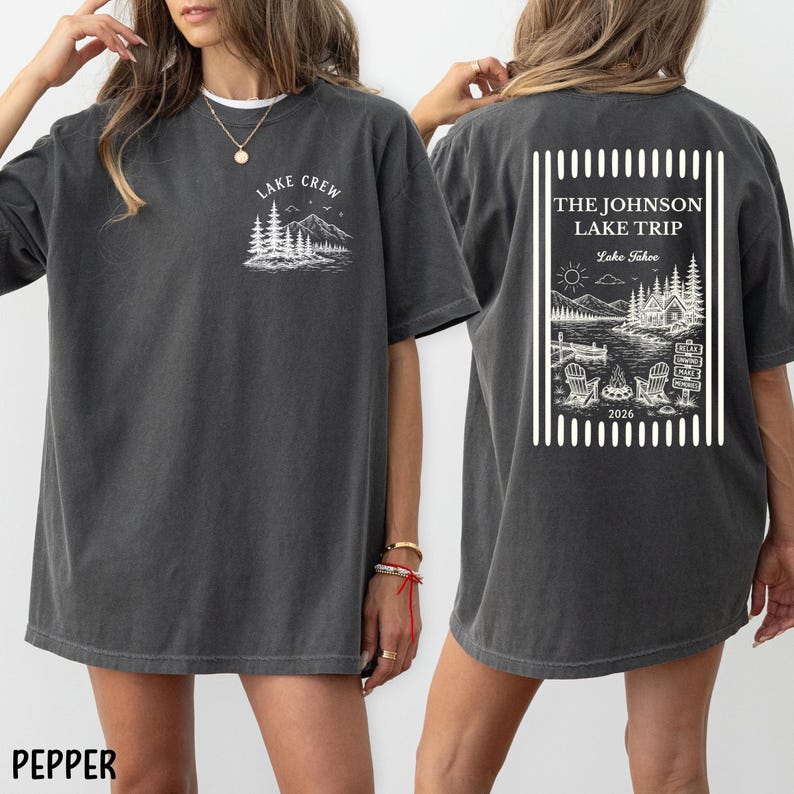 Puede incluir: Camiseta color pimienta con un gr&aacute;fico blanco en la parte delantera que dice "Lake Crew" con un dise&ntilde;o de monta&ntilde;a y &aacute;rboles. La parte posterior de la camisa tiene un dise&ntilde;o rectangular con el texto "The Johnson Lake Trip Lake Tahoe 2026".
