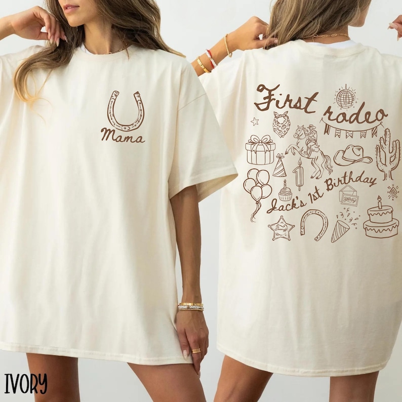 K&ouml;nnte beinhalten: Elfenbeinfarbenes T-Shirt mit einem Hufeisen und dem Wort "Mama" in Braun aufgedruckt. Die R&uuml;ckseite des Shirts zeigt ein "First rodeo"-Design mit einem Pferd, Kuchen, Luftballons und anderen Illustrationen zum Thema Rodeo. "Jack's 1st Birthday" ist ebenfalls auf der R&uuml;ckseite aufgedruckt.