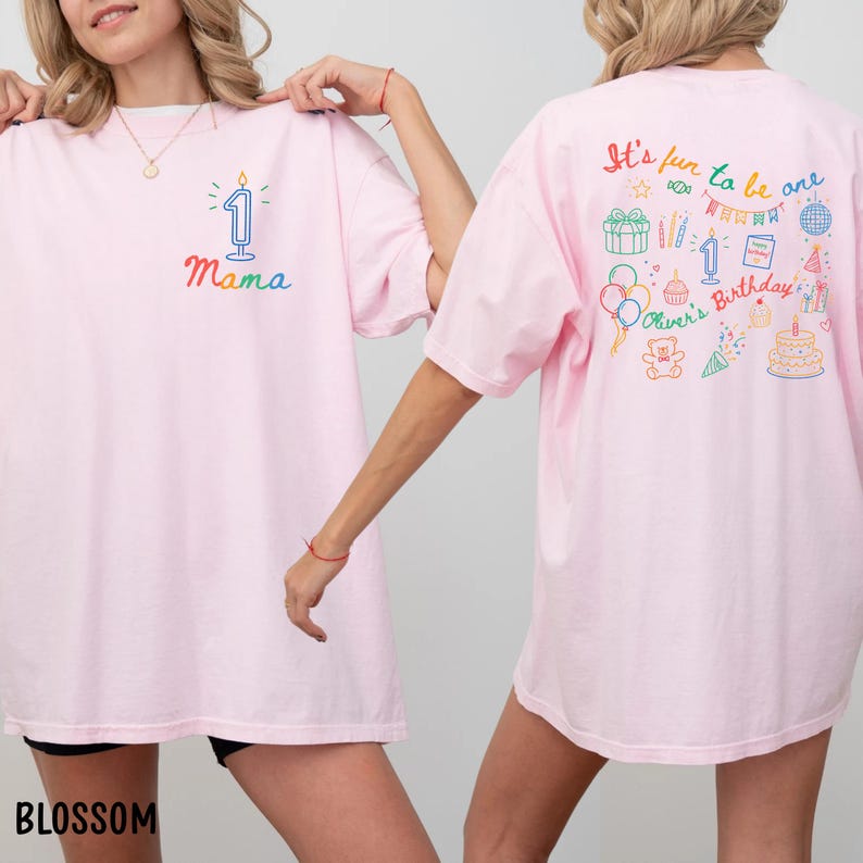 May include: Light pink t-shirts with colorful birthday-themed graphics. One shirt features a candle with the number one and the word "Mama". The other shirt has the text "It's fun to be one" and birthday-related illustrations.