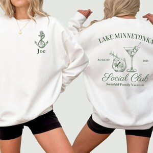 May include: White sweatshirt with a green anchor graphic and the name "Joe". The back of the sweatshirt features a cocktail design with the text "Lake Minnetonka Social Club" and "August 2025".