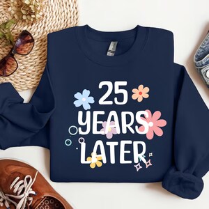 May include: Navy blue sweatshirt with white text that reads "25 years later" surrounded by colourful flowers.
