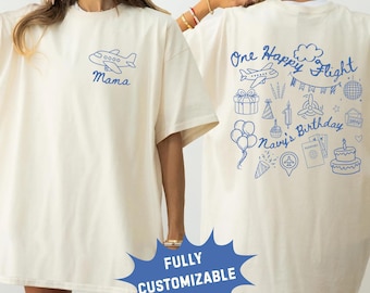 May include: Ivory-colored t-shirt with a blue airplane graphic and the word "Mama". The back of the shirt features the text "One Happy Flight Navy's Birthday" with various travel-themed illustrations.