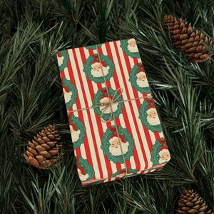May include: A wrapped gift with red and white striped paper, adorned with Santa Claus wreath patterns. The gift is tied with twine and rests on a bed of green pine needles and pine cones, creating a festive holiday scene.