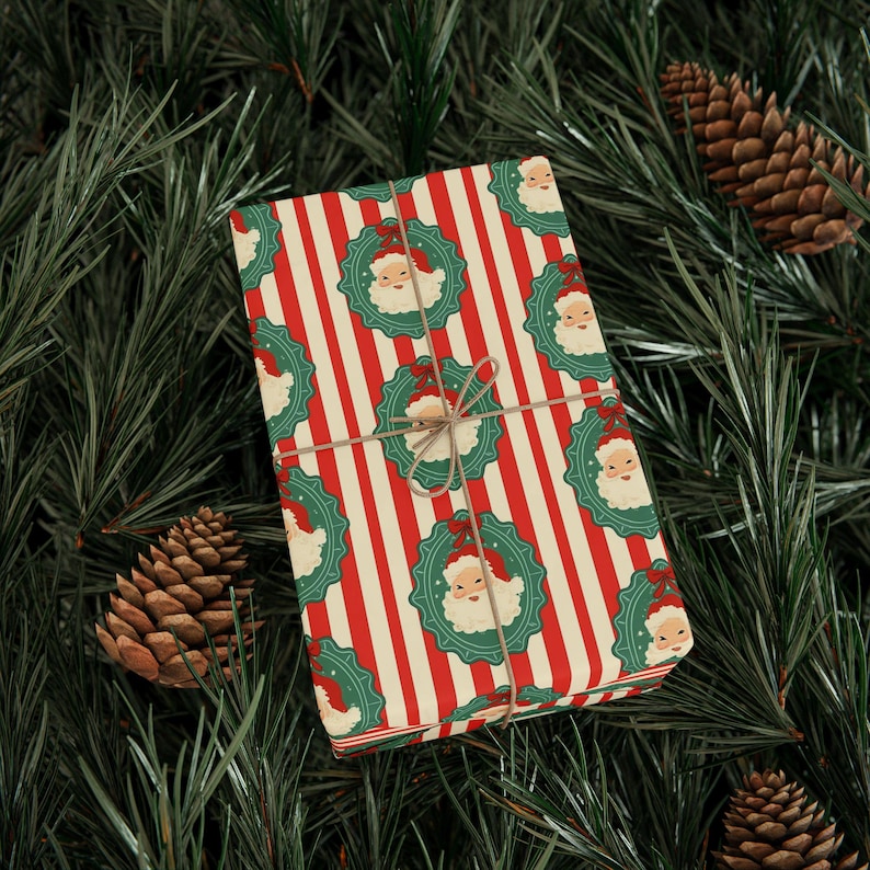 May include: A wrapped gift with red and white striped paper, adorned with Santa Claus wreath patterns. The gift is tied with twine and rests on a bed of green pine needles and pine cones, creating a festive holiday scene.