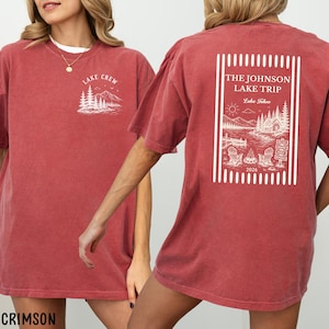 Puede incluir: Camisetas color carmes&iacute; con dise&ntilde;os gr&aacute;ficos blancos. Una camiseta presenta "LAKE CREW" con una escena de monta&ntilde;a y &aacute;rboles. La otra muestra "THE JOHNSON LAKE TRIP Lake Tahoe 2026" con una escena de lago, sillas y una fogata.