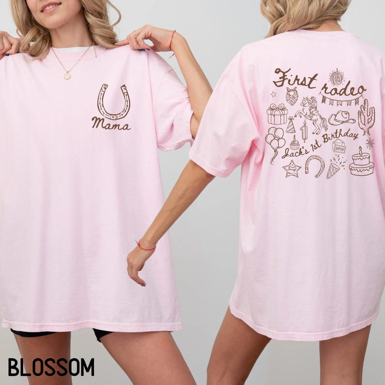 K&ouml;nnte beinhalten: Hellrosa T-Shirt mit einem braunen Hufeisen und dem Wort "Mama" auf der Vorderseite. Auf der R&uuml;ckseite des Shirts befindet sich ein "First Rodeo"-Design mit Geburtstagsthema, einschlie&szlig;lich Kuchen, Luftballons und Cowboyhut.