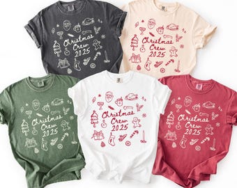 May include: Five t-shirts in different colours, including black, green, white, cream, and red. Each shirt displays a white graphic design with Christmas-themed illustrations and the text "Christmas Crew 2025".