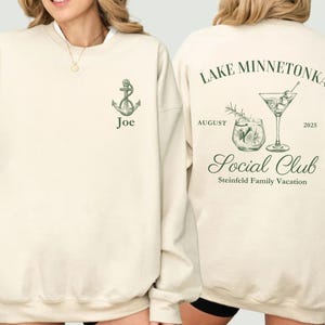 May include: Cream-colored sweatshirt with green anchor graphic and the name "Joe". The back features "Lake Minnetonka Social Club" text, cocktail illustrations, and "August 2025". Steinfield Family Vacation is also printed on the back.