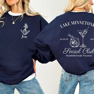 May include: Navy blue sweatshirt with white accents. The front features an anchor graphic and the name "Joe". The back displays "Lake Minnetonka Social Club" with cocktail illustrations, the month of August, and the year 2025. A family vacation theme.