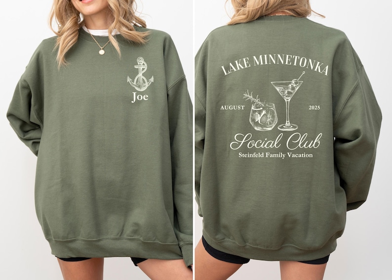 May include: Olive green sweatshirt with white graphic designs. The front features an anchor and the name "Joe." The back displays "Lake Minnetonka Social Club" with cocktail illustrations, the month of August, and the year 2025. Steinfield Family Vacation is also printed on the back.