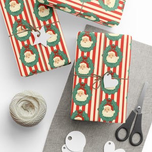 May include: Christmas-themed gift wrap with a red and white striped pattern. The paper features a repeating design of Santa Claus faces in green wreaths. Gifts are tied with twine and blank white tags. A ball of twine and scissors are also visible.