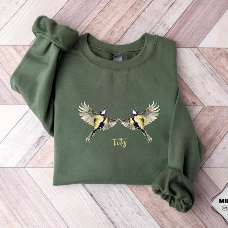 May include: A green sweatshirt with a graphic of two birds facing each other with the word "tits" printed below them.