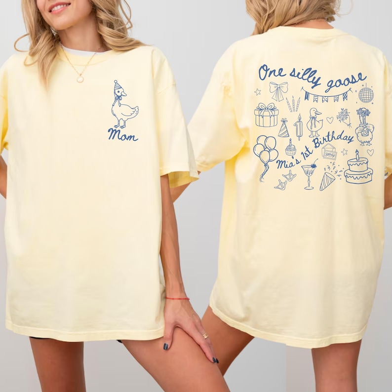 Peut inclure: T-shirt jaune clair avec un motif d'oie bleue et le mot "Mom" sur le devant. Le dos du t-shirt pr&eacute;sente le texte "One silly goose" et des illustrations sur le th&egrave;me de l'anniversaire, dont un g&acirc;teau et des ballons. Style d&eacute;contract&eacute;.