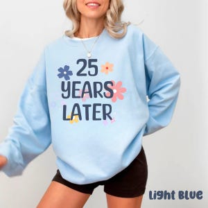 May include: Light blue sweatshirt with the text "25 years later" and floral designs.