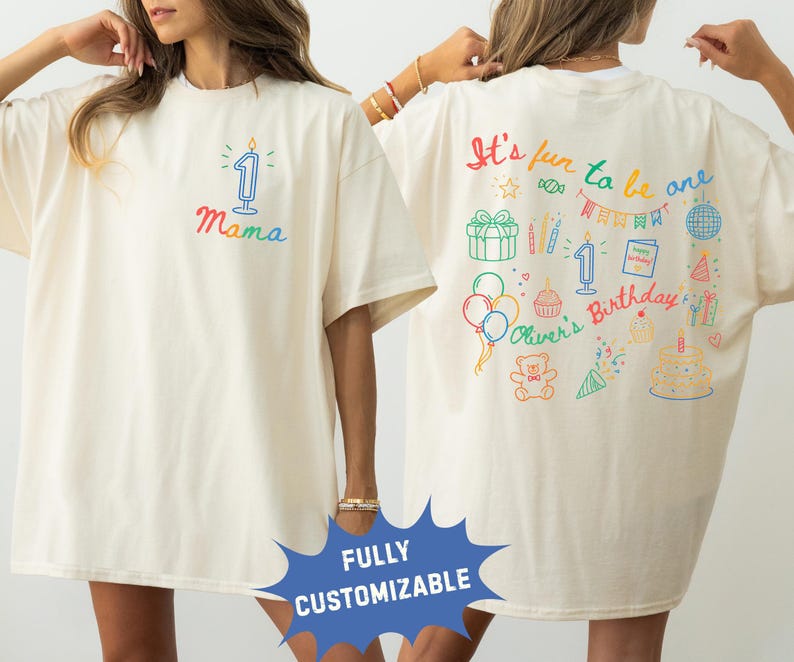 May include: Cream-colored t-shirt with colorful birthday-themed graphics. The front features a candle with the number 1 and the word "Mama". The back displays the text "It's fun to be one" and various birthday illustrations, including a cake and balloons.