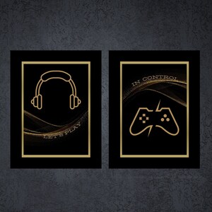 Puede incluir: Dos impresiones enmarcadas en negro con detalles dorados. La impresión de la izquierda presenta un contorno dorado de unos auriculares con el texto "Let's Play". La impresión de la derecha presenta un contorno dorado de un mando de videojuego con el texto "In Control".