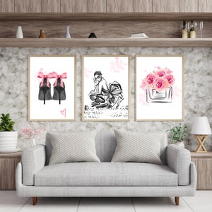 Peut inclure: Trois impressions encadrées dans un style aquarelle. La première impression représente une paire de talons hauts noirs avec des nœuds roses. La deuxième impression représente une femme en robe noire et talons hauts. La troisième impression représente un flacon de parfum avec des fleurs roses.