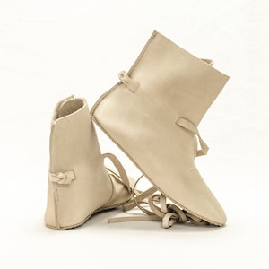 May include: Two pairs of beige leather ankle boots with laces. The boots are made of a soft, supple leather and have a simple, classic design.