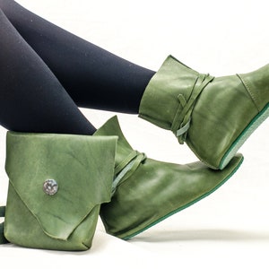 May include: A pair of green leather boots with laces and a pointed toe. The boots are worn with black tights.