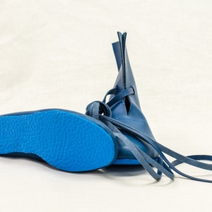 May include: A pair of blue leather boots with laces. The boots have a pointed toe and a flat sole.