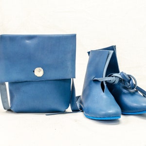 May include: A pair of blue leather boots with laces and a blue leather crossbody bag with a silver button.