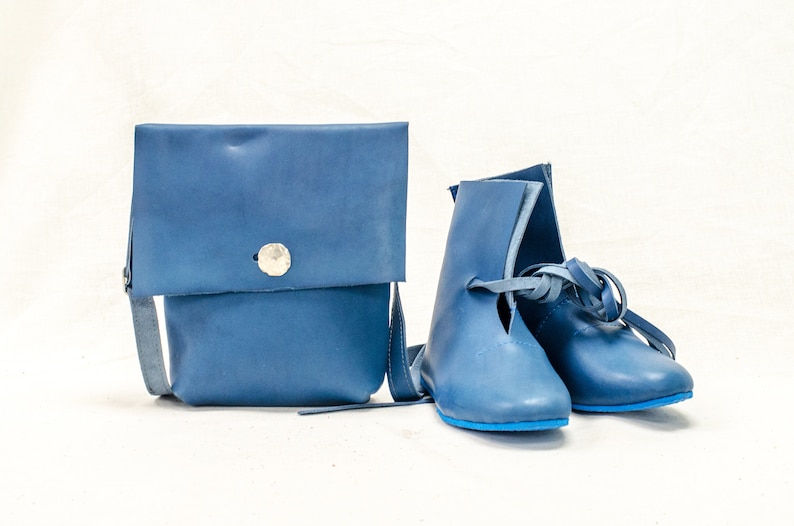 May include: A pair of blue leather boots with laces and a blue leather crossbody bag with a silver button.