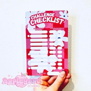 May include: A rectangular challenge checklist card featuring a red and pink checkered background with white flower graphics. The card includes text that reads CHALLENGE CHECKLIST, CHALLENGE, AMOUNT, COMPLETE, and TOTAL SAVED with blank spaces.