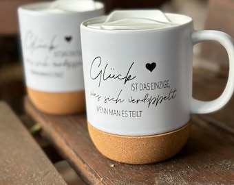 May include: Two white ceramic mugs with cork bottoms. The mug on the right has a black heart and the text "Glück ist das Einzige, was sich verdoppelt wenn man es teilt".