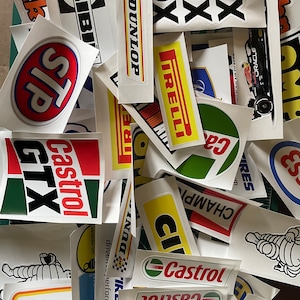 May include: A collection of vintage racing car stickers featuring various brands such as Castrol, Dunlop, and Pirelli. The stickers are printed on white paper with colourful logos and text.