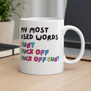 Puede incluir: Taza de cerámica blanca con el texto "MY MOST USED WORDS" en negro, y las palabras "CUNT", "FUCK OFF" y "FUCK OFF CUNT" en letras coloridas. La taza tiene un asa curva.