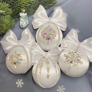 May include: Four white satin Christmas ornaments with jeweled snowflake designs. Each ornament is adorned with a white satin bow.
