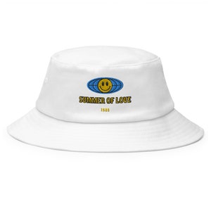 May include: White bucket hat with a blue and yellow smiley face graphic and the text "SUMMER OF LOVE 1988"