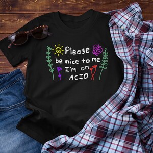 May include: Black t-shirt with a colorful graphic that says "Please be nice to me I'm on ACID". The graphic features a sun, flowers, and a butterfly.