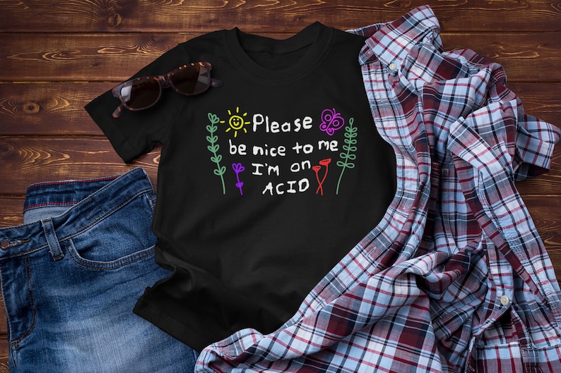 May include: Black t-shirt with a colorful graphic that says "Please be nice to me I'm on ACID". The graphic features a sun, flowers, and a butterfly.